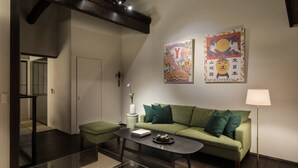 Una sala de estar moderna con un sofá verde, una mesa de centro negra y una lámpara de pie. Hay dos adornos de pared y un pequeño jarrón blanco con una planta.