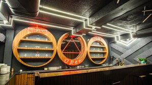 Un bar doté de trois étagères en bois, chacune portant l’inscription « The Open », et sur lesquelles sont disposés des verres et des bouteilles.