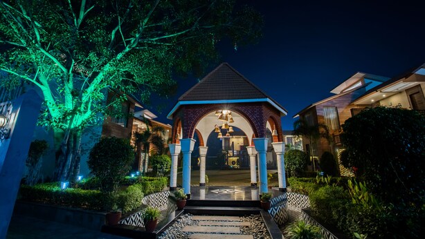 Vue nocturne d’un bâtiment doté d’un pavillon central, entouré d’une végétation luxuriante et illuminé par un éclairage vert.