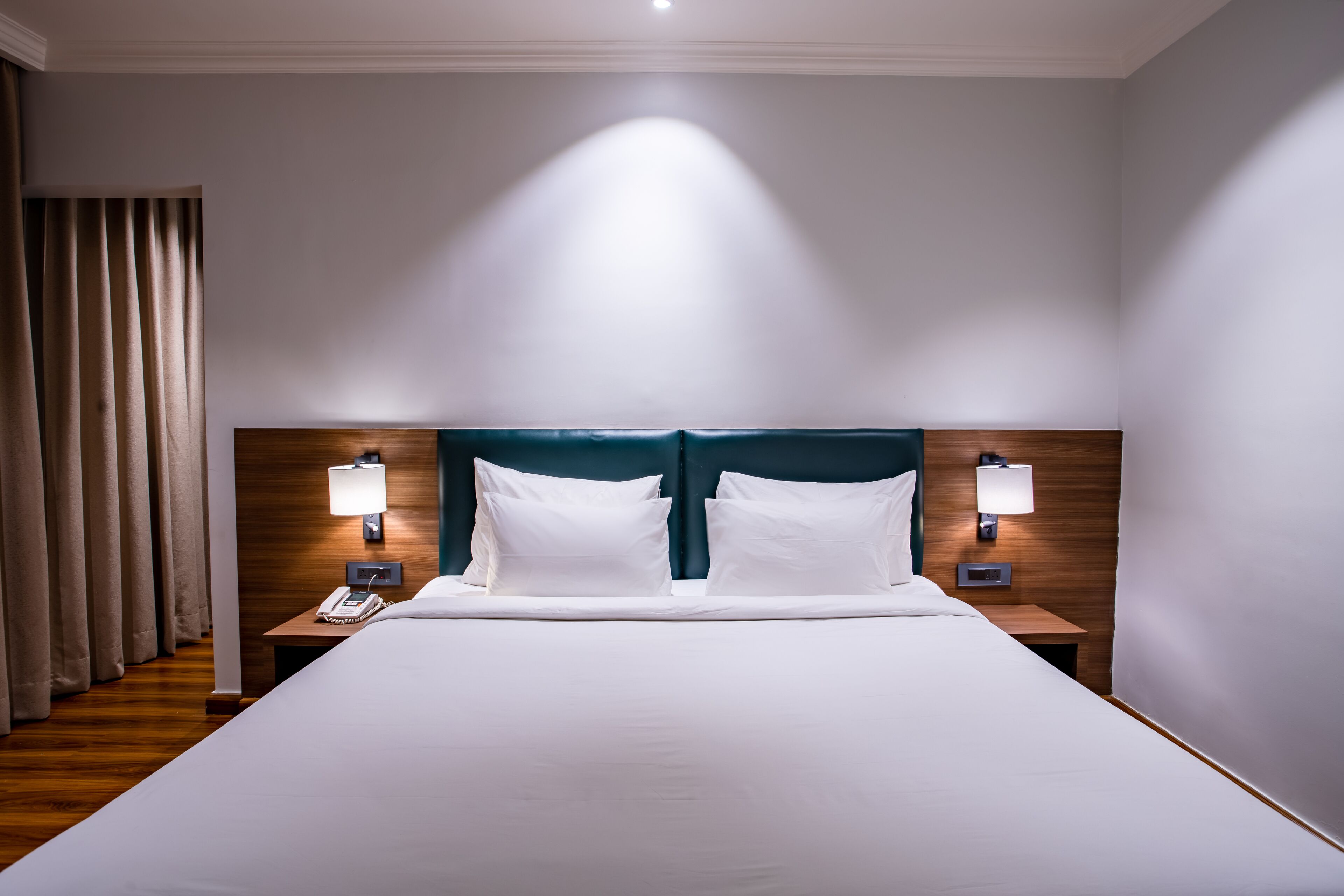 A hotel room with a large bed, two bedside lamps, a telephone, and a curtain.