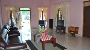 A living room with a sofa, a coffee table with flowers, a television, and speakers. - Dil Lanka Safari Resort (Udawalawa)