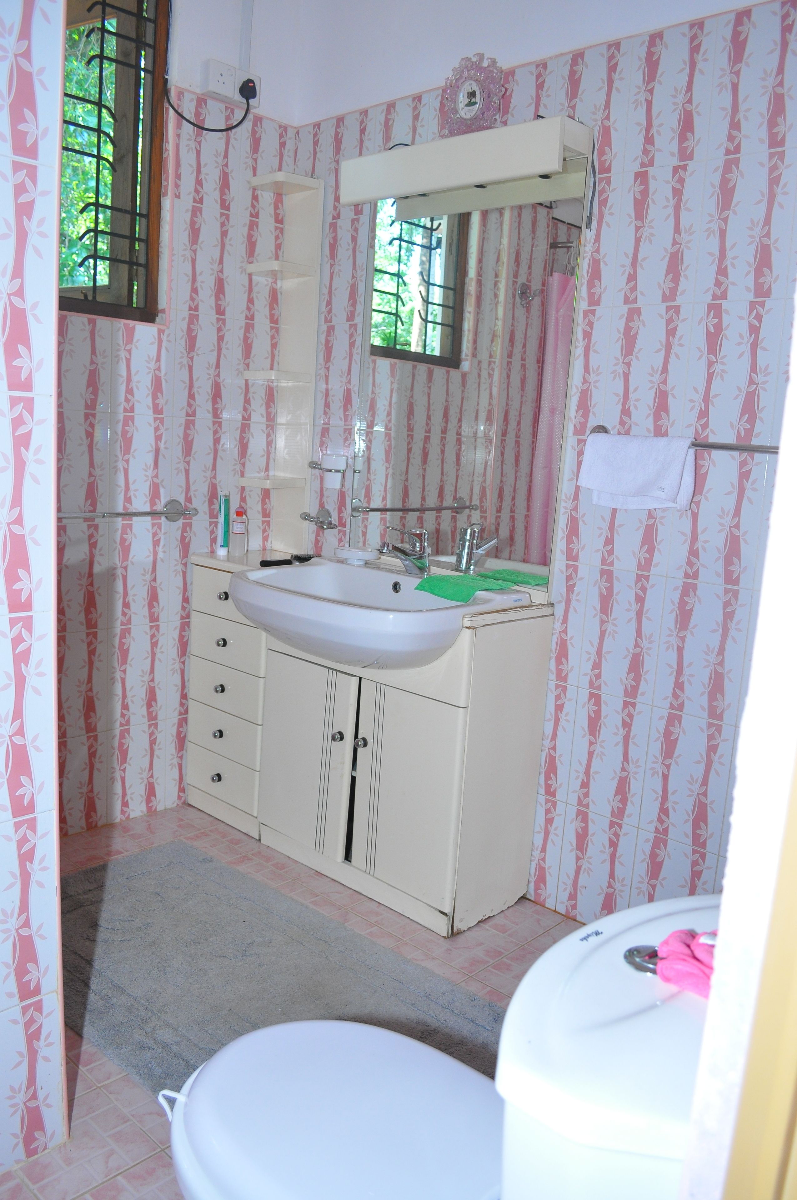 A bathroom with a white sink, mirror, and toilet. There is a window with bars and a towel rack with a towel.