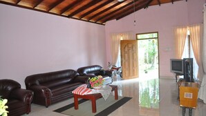 A living room with a brown leather sofa, a wooden coffee table with a red and white striped tablecloth, and a television on a wooden stand. - Dil Lanka Safari Resort (Udawalawa)