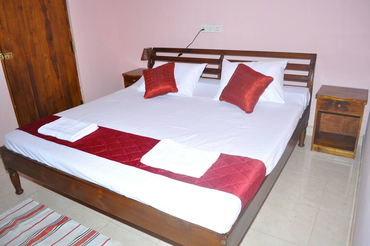 Una cama bien hecha con estructura de madera, ropa de cama blanca y roja, y una manta roja.