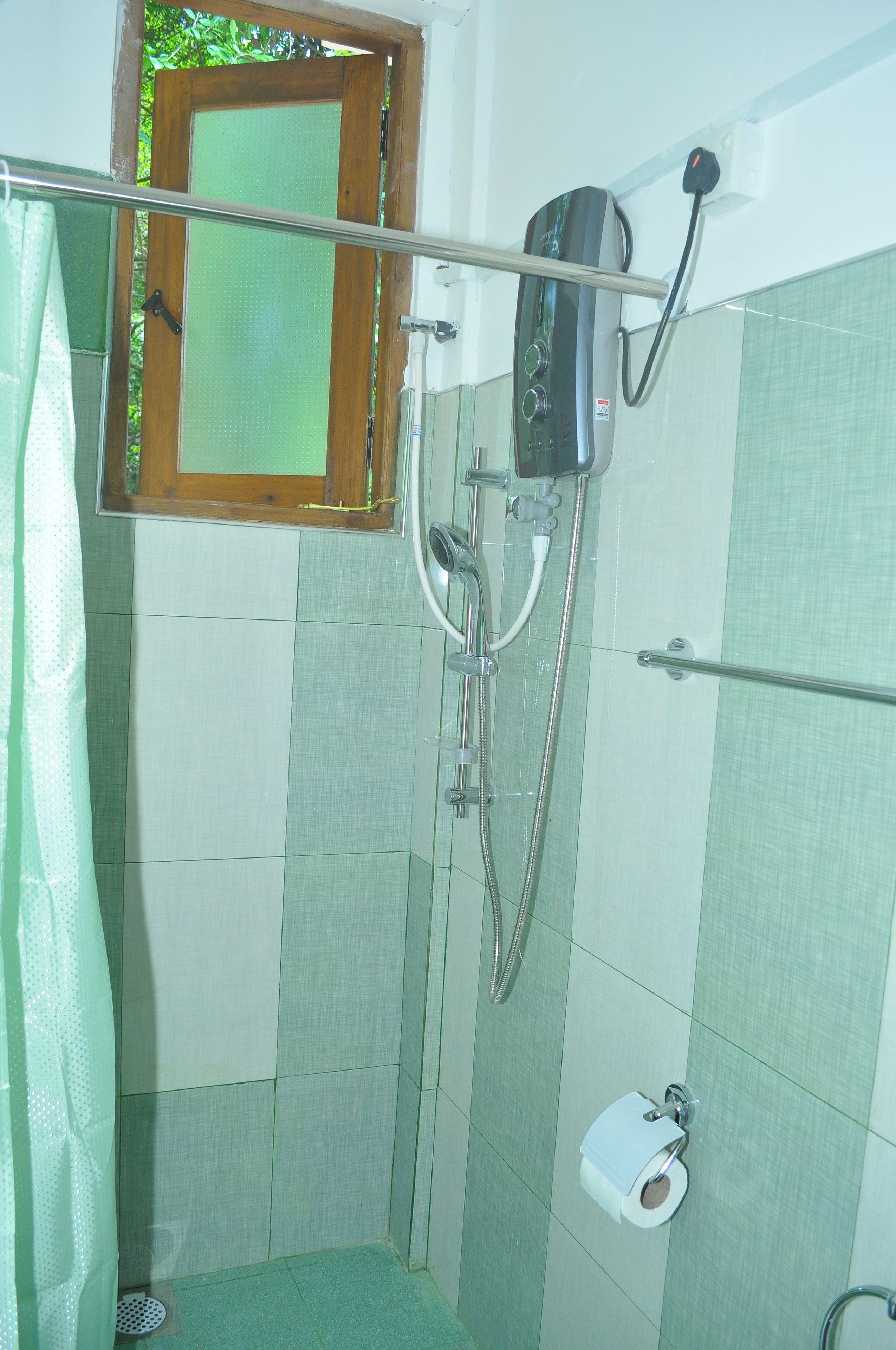 Chuveiro com chuveiro manual, porta de vidro e vaso sanitário com suporte para papel toalha.