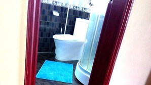 Une salle de bain avec des toilettes blanches, un tapis de bain bleu et un espace douche.