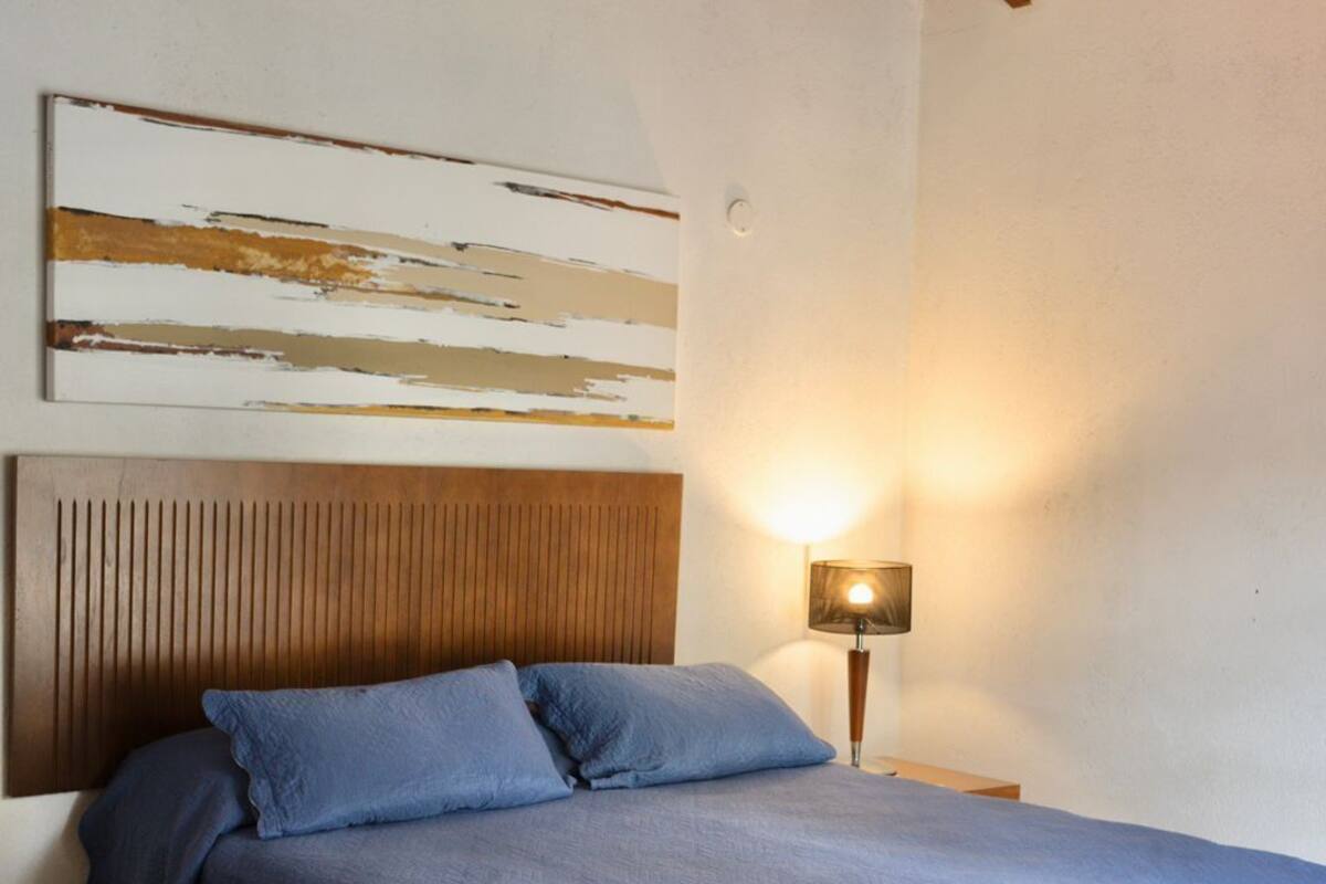 A bedroom with a bed, a headboard, a wall-mounted artwork, and a bedside lamp.
