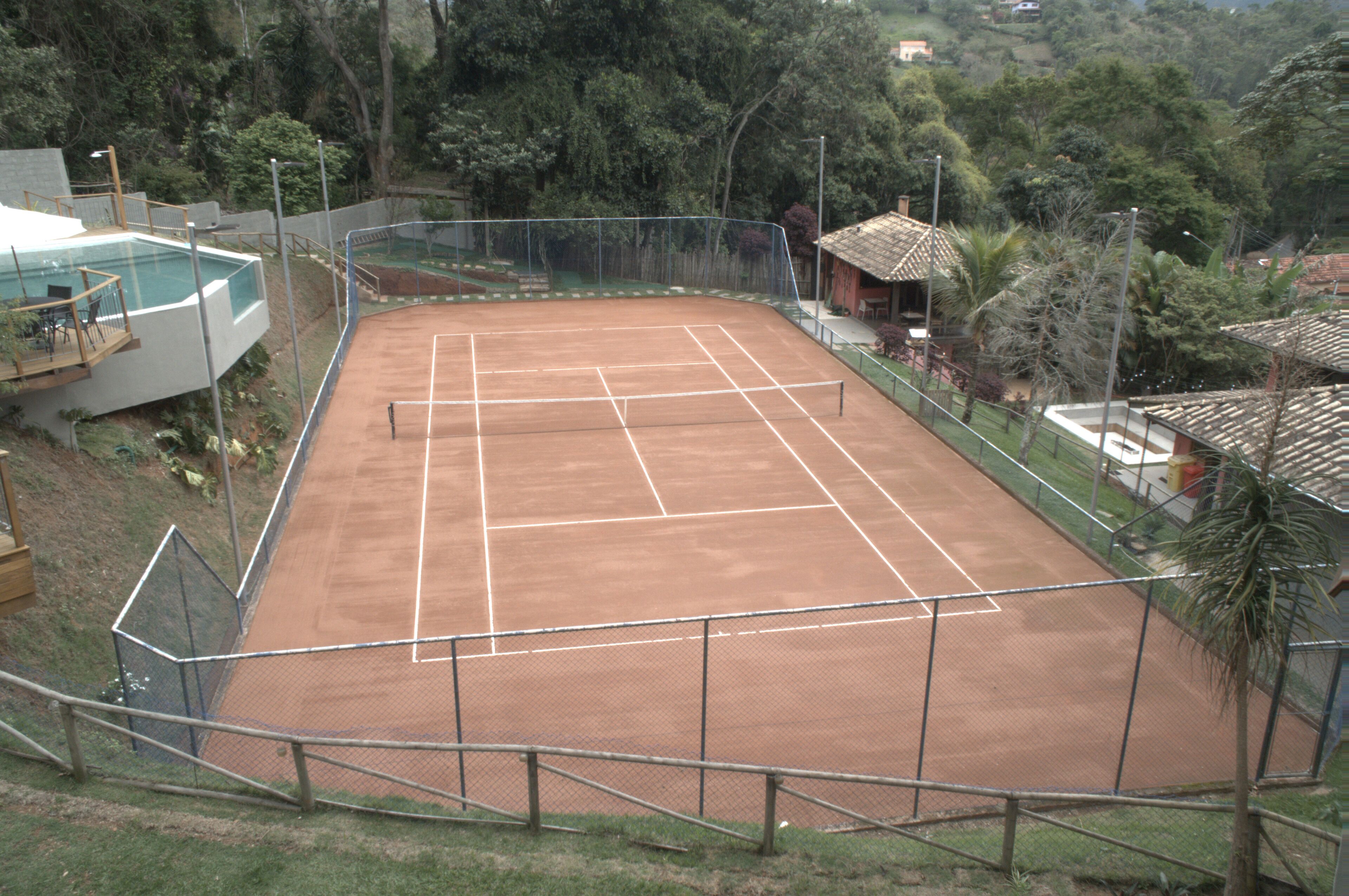 Ein Tennisplatz, umzäunt, mit einem Pool und einem kleinen Gebäude in der Nähe.