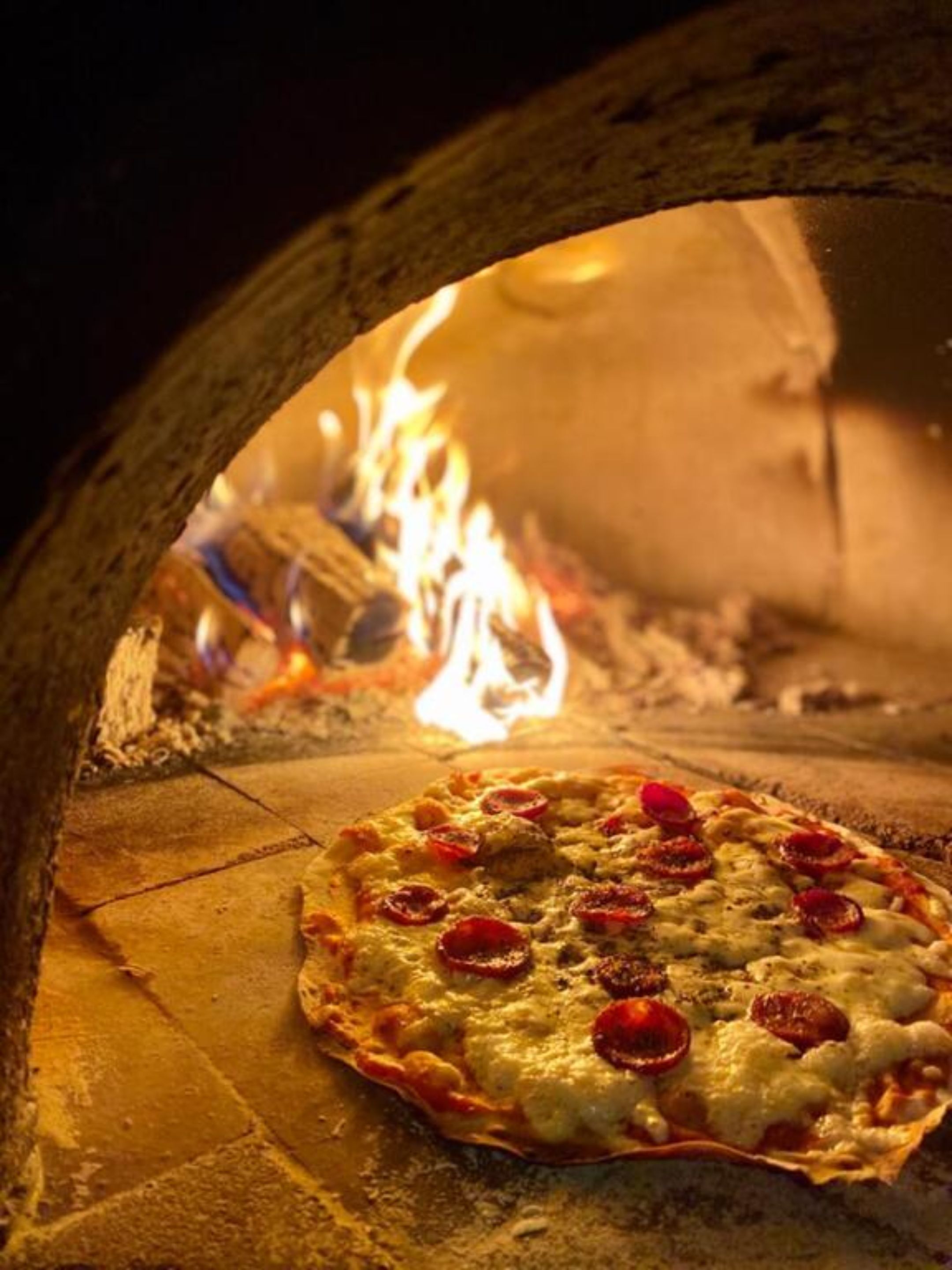 A pizza in a wood-fired oven with visible flames.