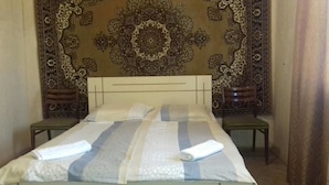 A neatly made bed with a striped bedspread and two rolled towels, a wooden headboard, and a decorative wall hanging. - Farmer's Guest House (Telavi)