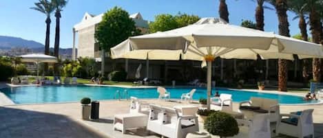 Una piscina al aire libre, sombrillas, sillones reclinables de piscina