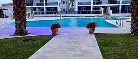 Una piscina al aire libre, sombrillas, sillones reclinables de piscina