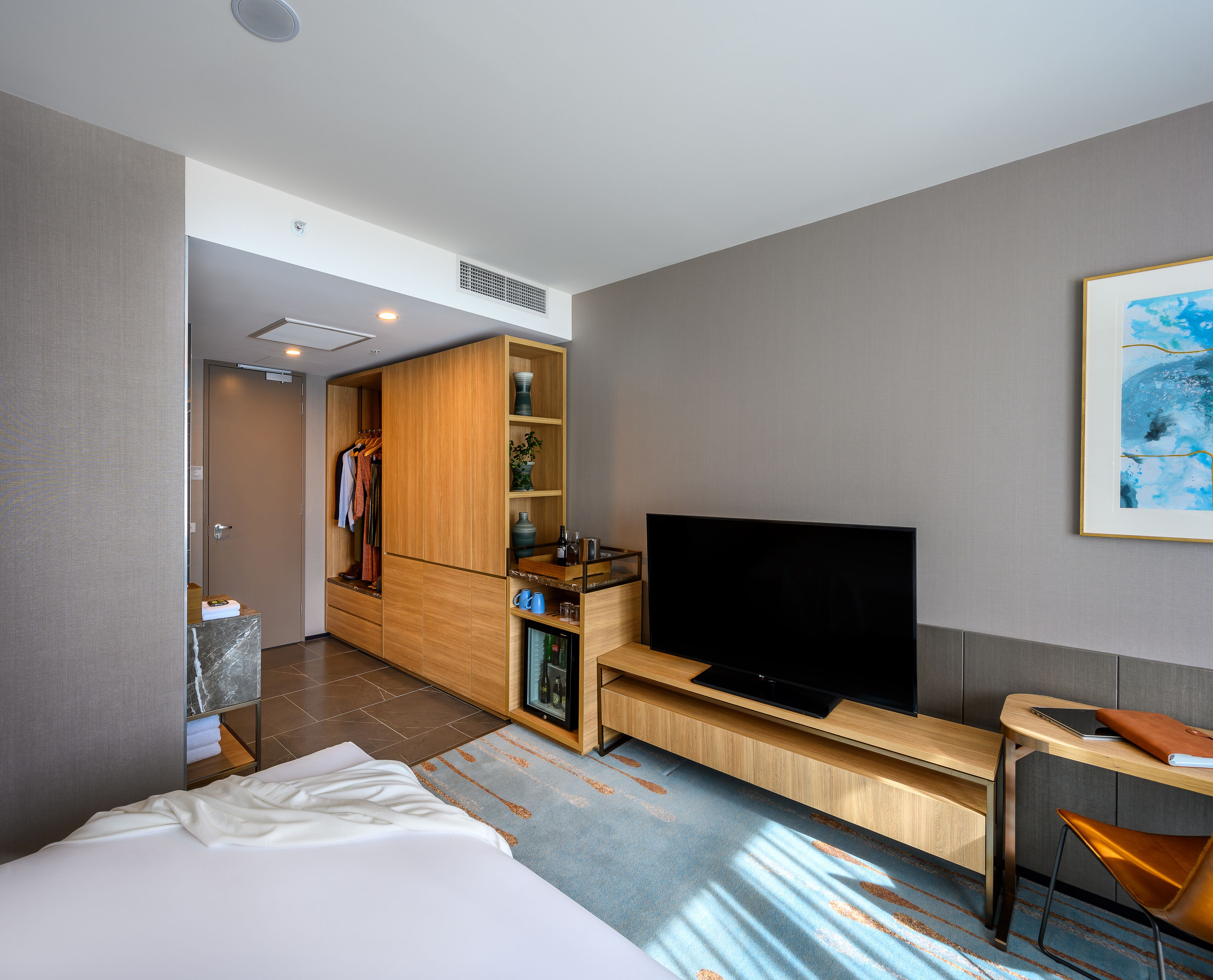 A modern hotel room with a bed, a TV, a desk, and a wardrobe.