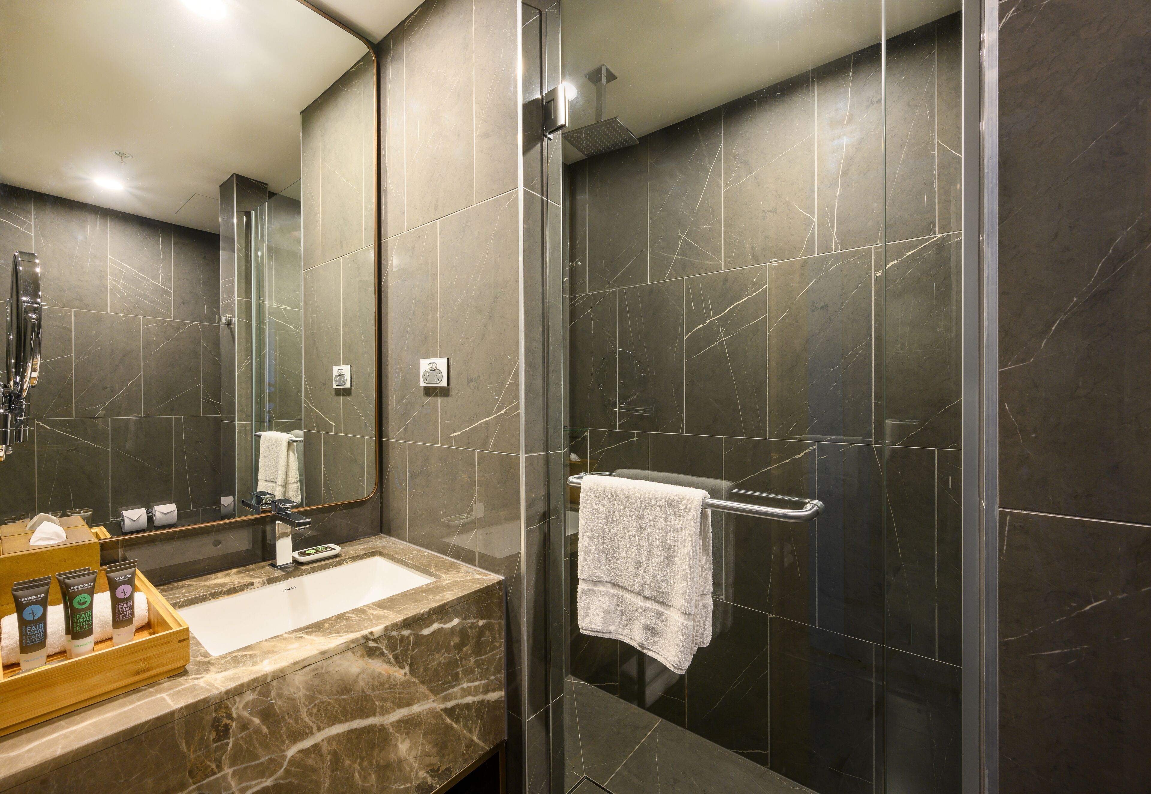 A modern bathroom with a glass-enclosed shower, a marble sink, and a wooden tray with toiletries.