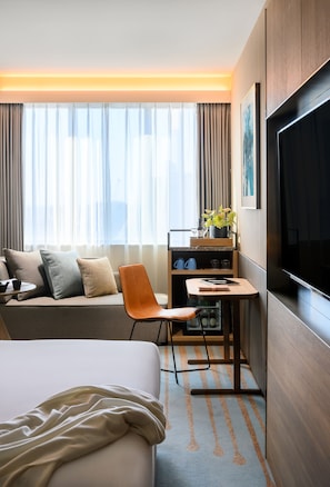 A hotel room with a bed, a desk, a chair, a TV, and a window with curtains.