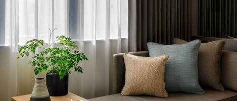A modern hotel room with a sofa, a small table with a plant, and a window with sheer curtains.