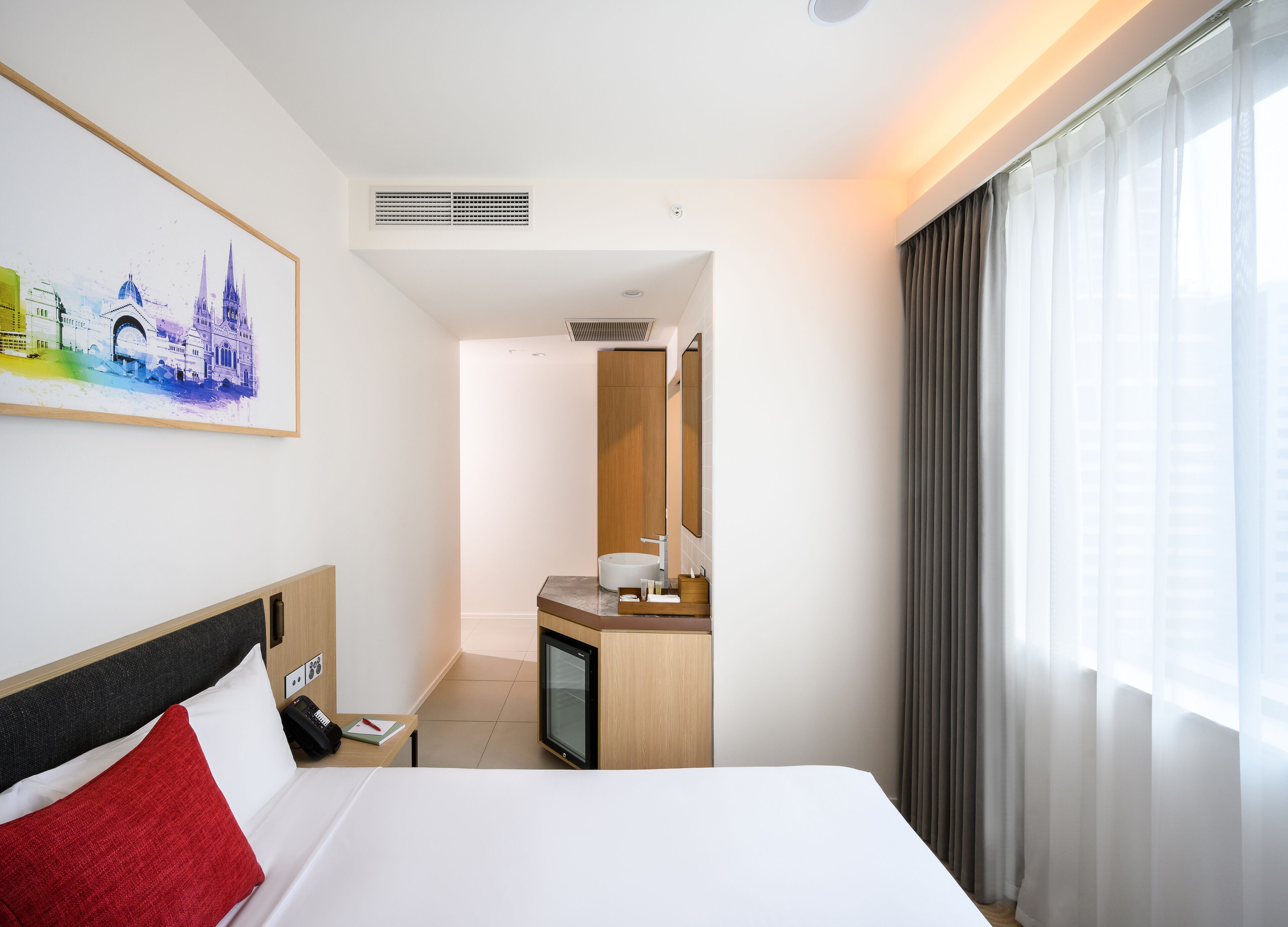 Quarto de hotel com cama, secretária com computador, banheiro e um quadro na parede.