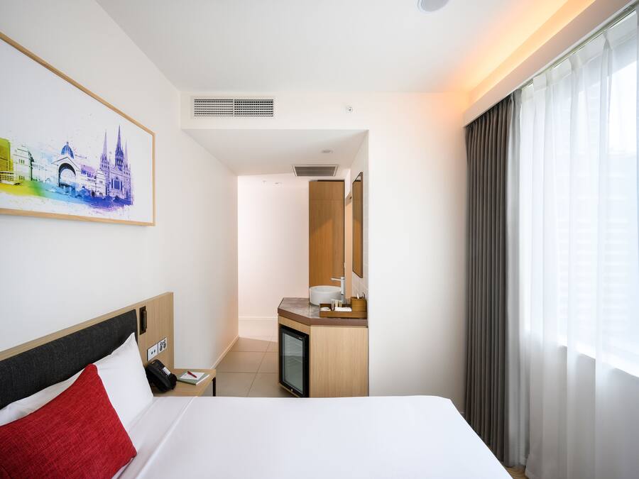 Quarto de hotel com cama, secretária com computador, banheiro e um quadro na parede.