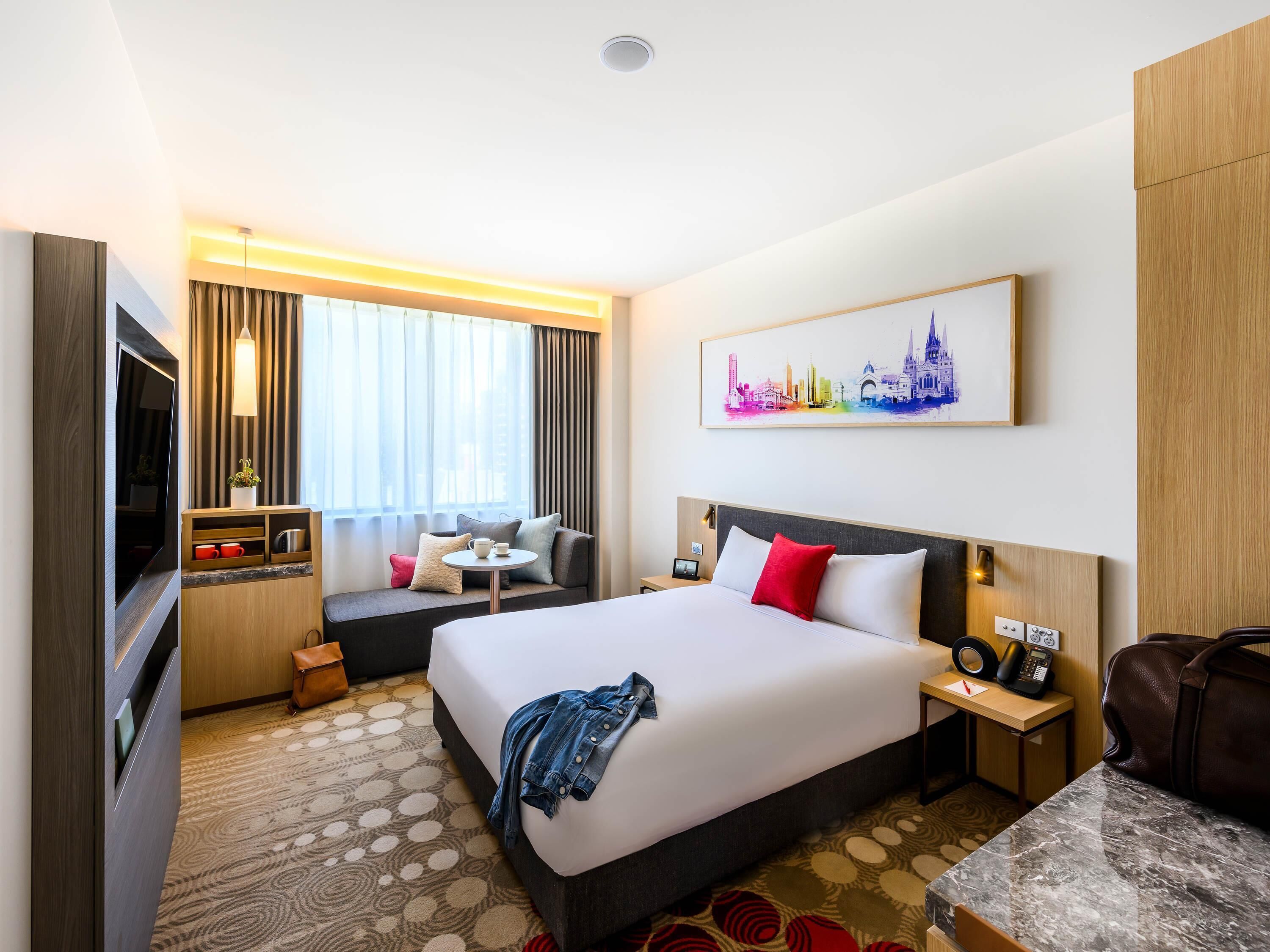 A hotel room with a bed, a sofa, a TV, a desk, and a painting on the wall.
