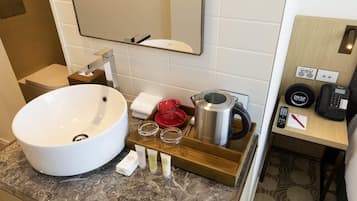 Une salle de bain avec un grand lavabo blanc, un miroir, un plateau en bois contenant des articles de toilette, une bouilloire et une horloge.