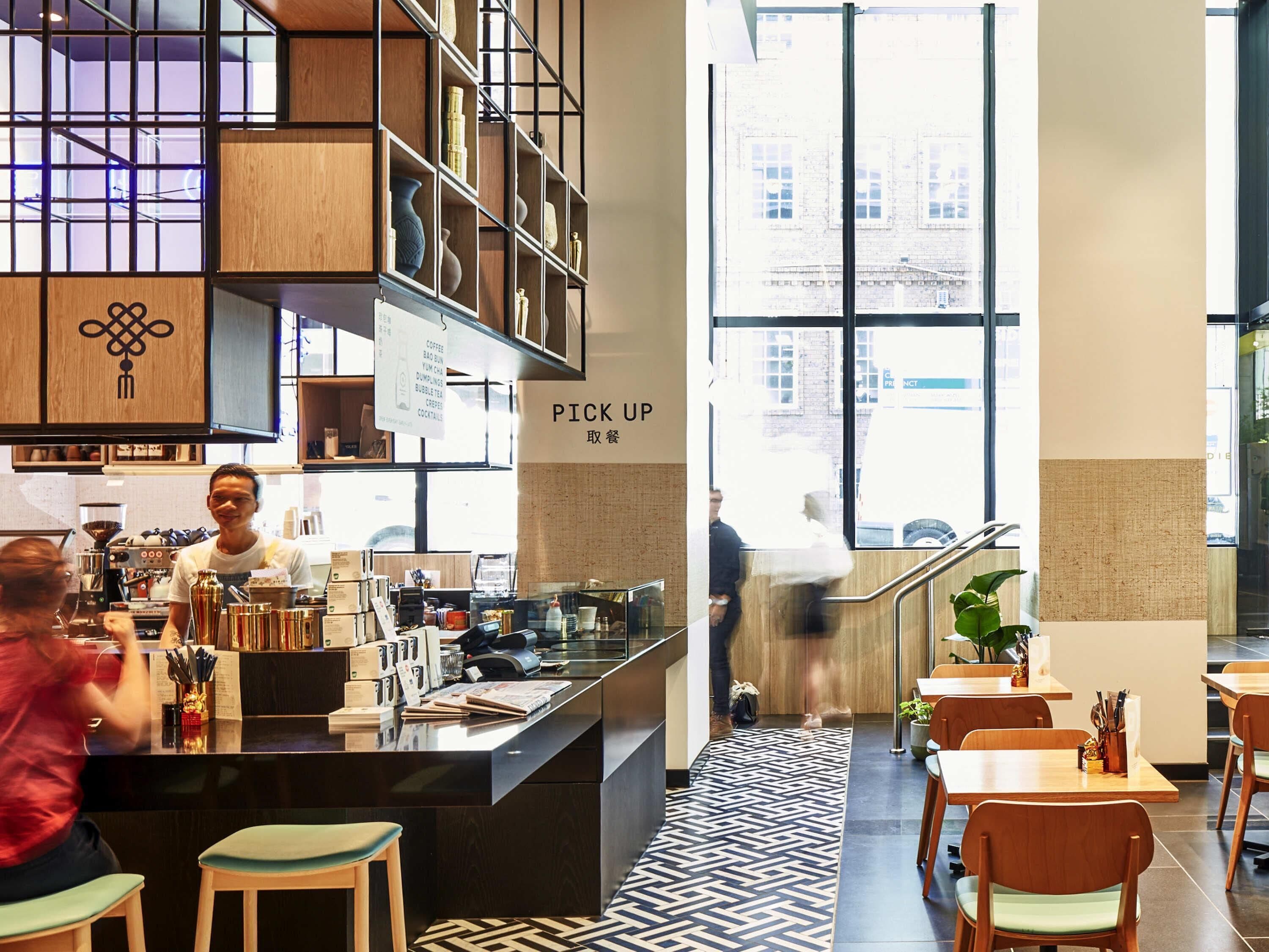 Interior moderno de una cafetería con mostrador, zona de estar y grandes ventanales.