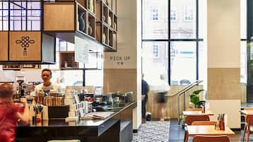 Interior moderno de una cafetería con mostrador, zona de estar y grandes ventanales.