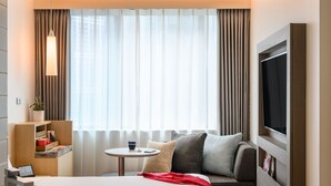 Una habitación de hotel moderna con una cama, televisi ón, una mesita y un baño con lavamanos y espejo.