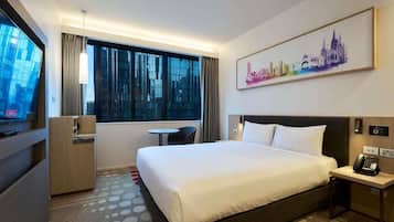 A hotel room with a large bed, a desk, a chair, a window with curtains, a painting on the wall, and a cityscape view.