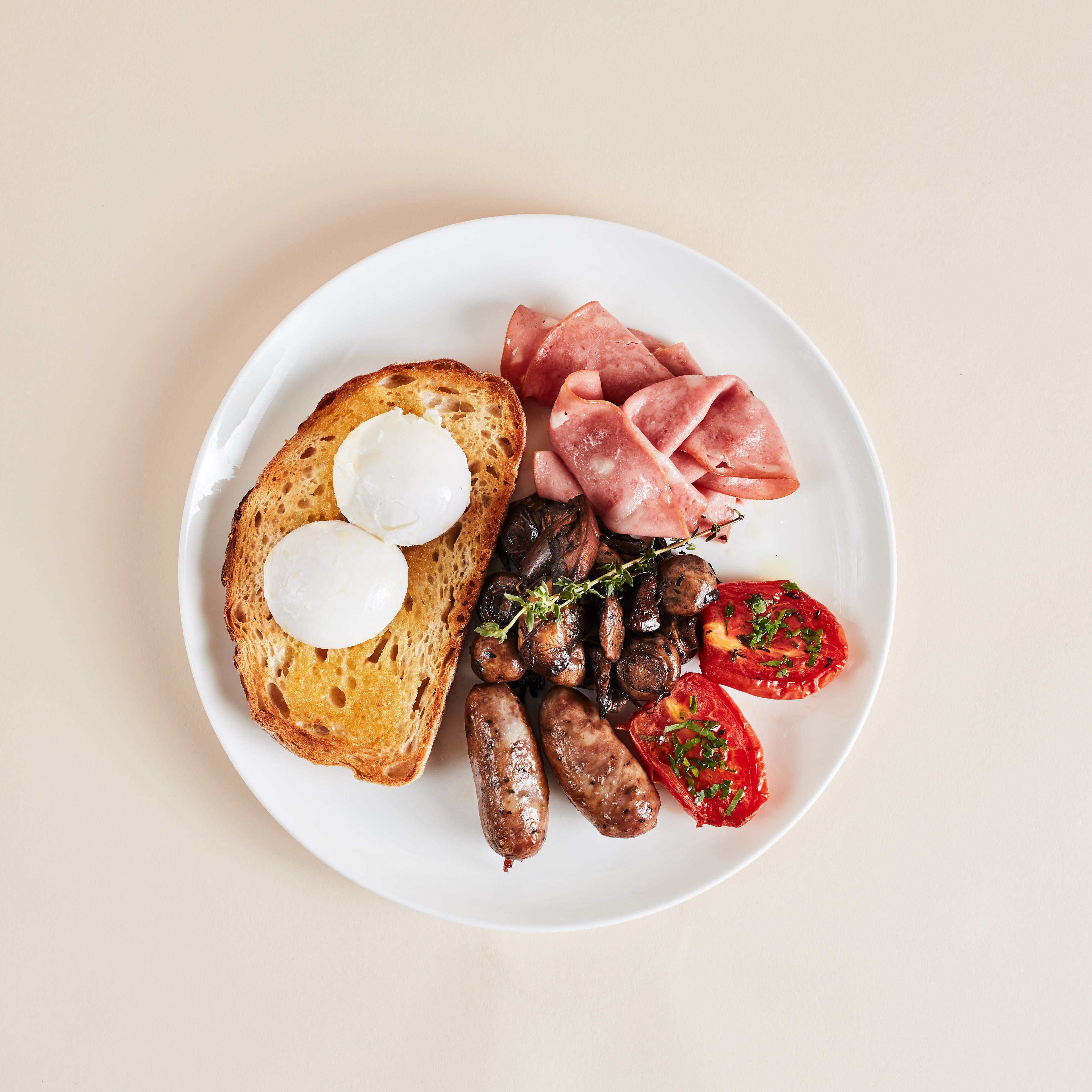 Ein Teller mit Toast, Eiern, Würstchen, Schinken, Pilzen und Tomaten.