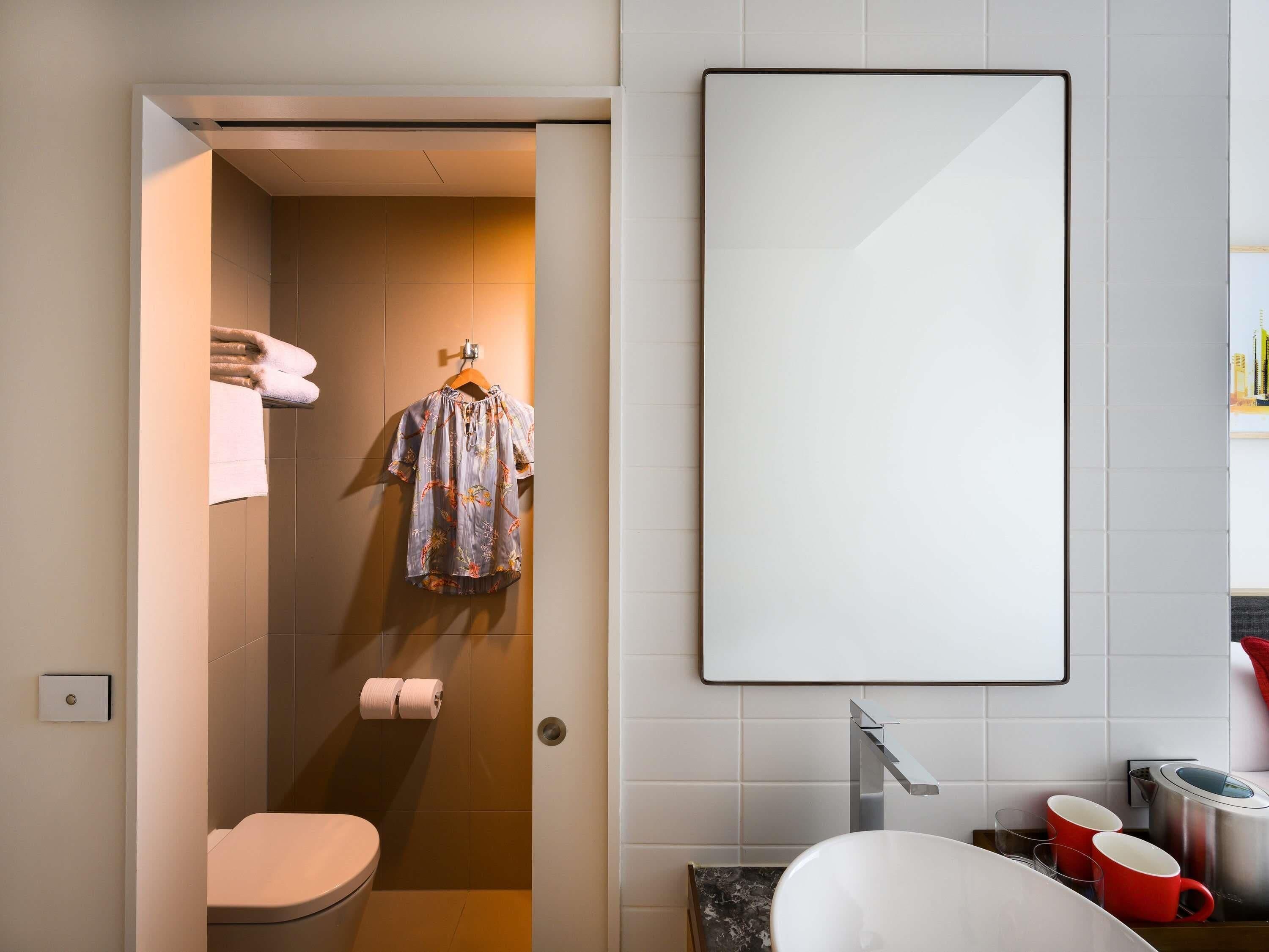 A modern bathroom with a toilet, shower, and a large mirror.