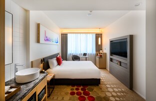 A hotel room with a large bed, a TV, a desk, and a bathroom with a sink and mirror.