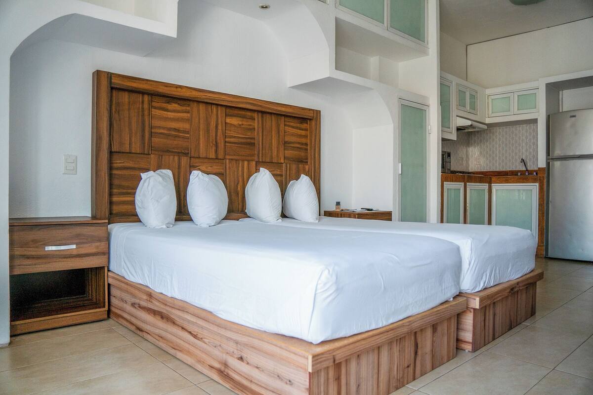 Een slaapkamer met een houten hoofdbord, een groot bed met witte beddengoed, een nachtkastje en een inbouwbank.