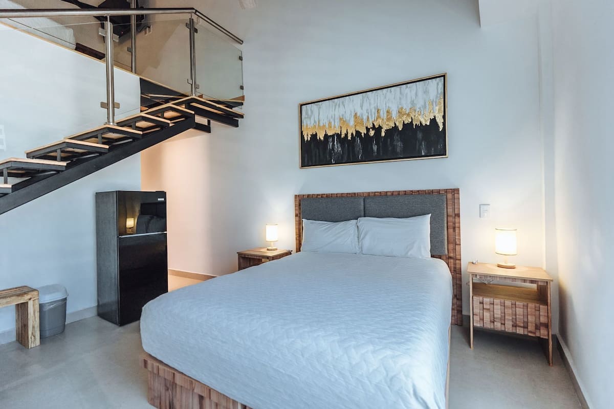 Een slaapkamer met een bed, nachtkastjes, een aan de muur hangend schilderij, een trap en een koelkast.