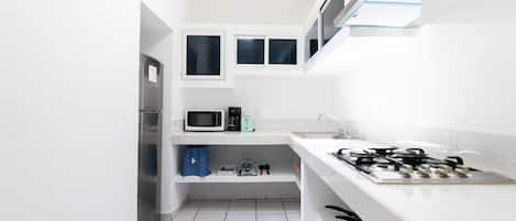 A compact kitchen with white cabinets, a microwave, a gas stove, and a sink.