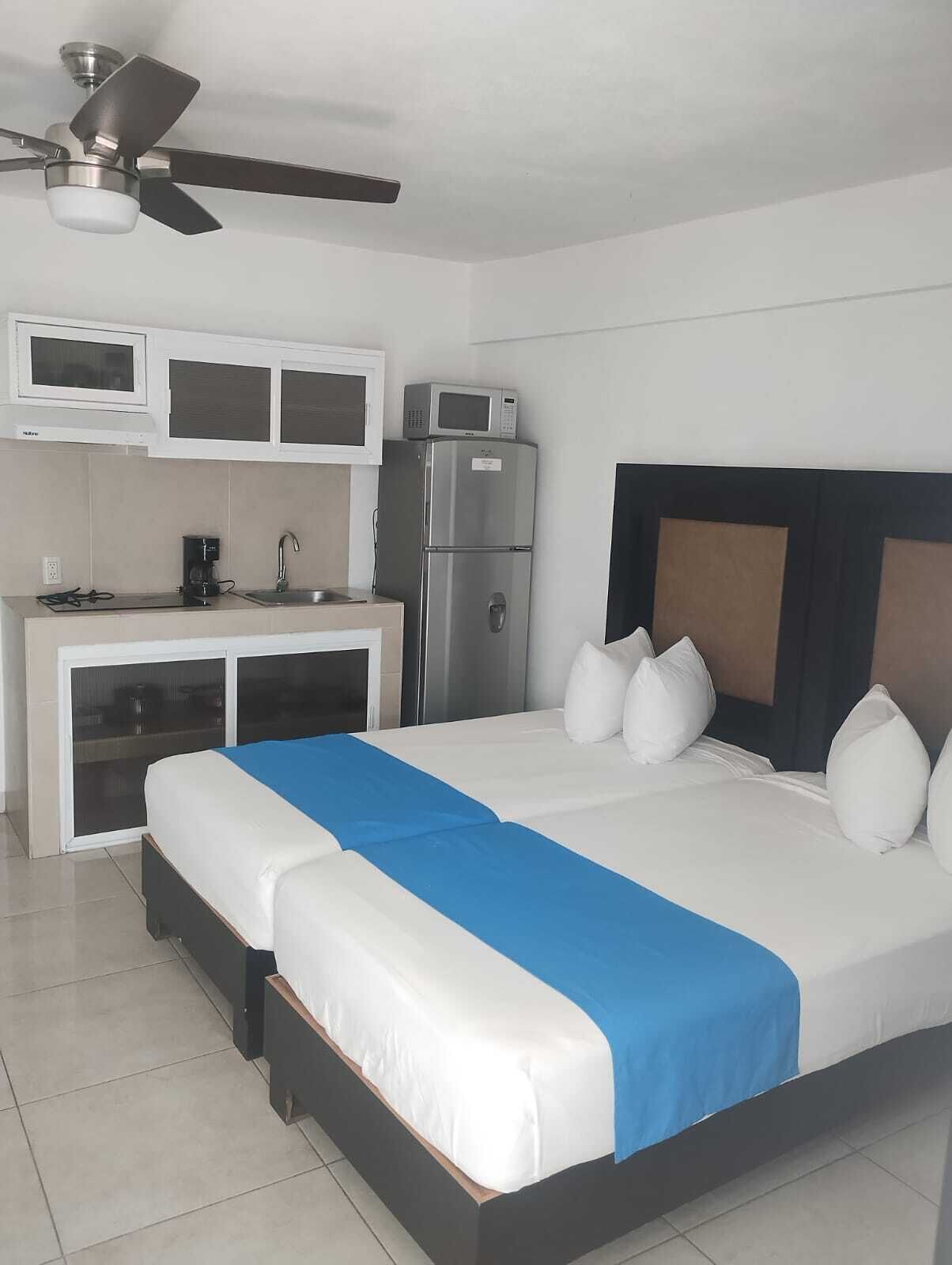 Habitación de hotel con cama, escritorio, microondas, refrigerador y ventilador de techo.