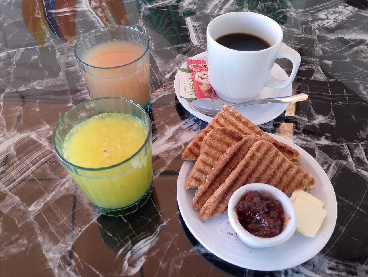 Une table en marbre dressée pour le petit-déjeuner, avec un verre de jus d’orange, une tasse de café, des gaufres, du beurre et de la confiture.