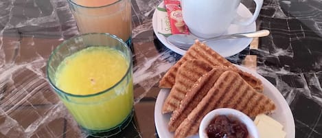 A breakfast setting with a glass of orange juice, a cup of coffee, waffles, butter, and jam on a marble table.