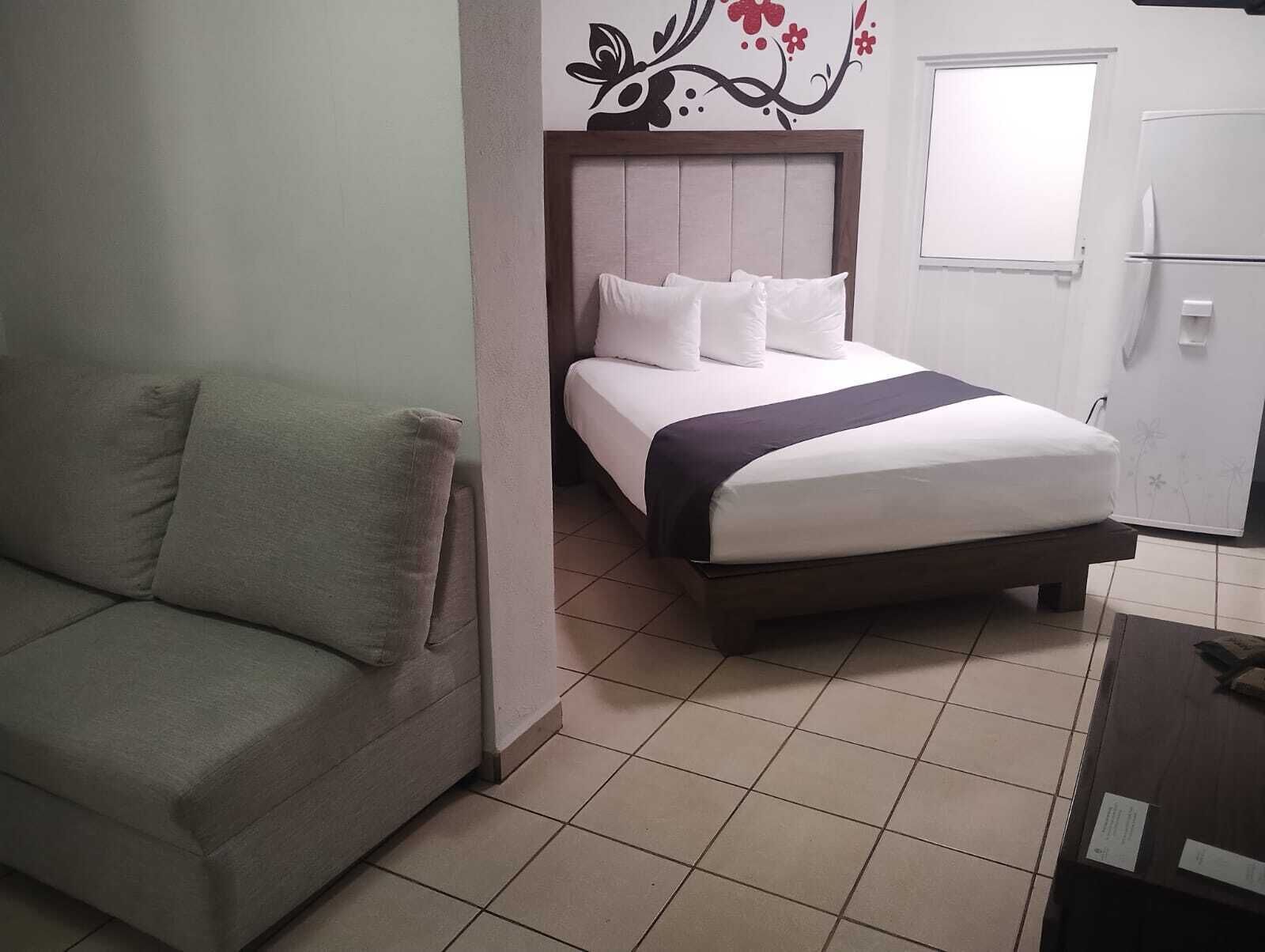 Un dormitorio con cama, sofá, ventana y refrigerador.