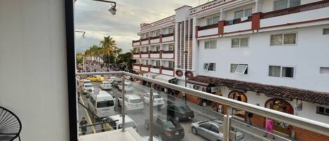 Un balcón con vistas a una calle concurrida, un edificio de varios pisos y un cielo despejado.