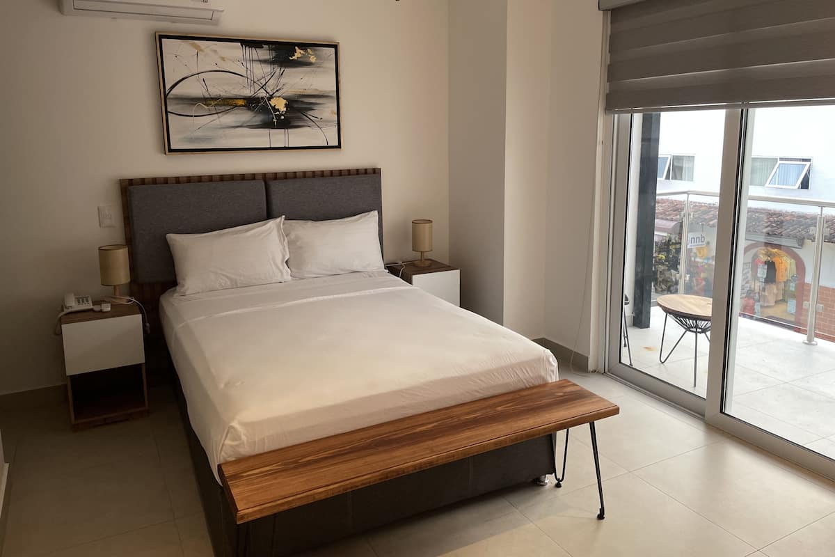 Een moderne slaapkamer met een groot bed, nachtlampjes, een plafondventilator en uitzicht op de stad door grote ramen.