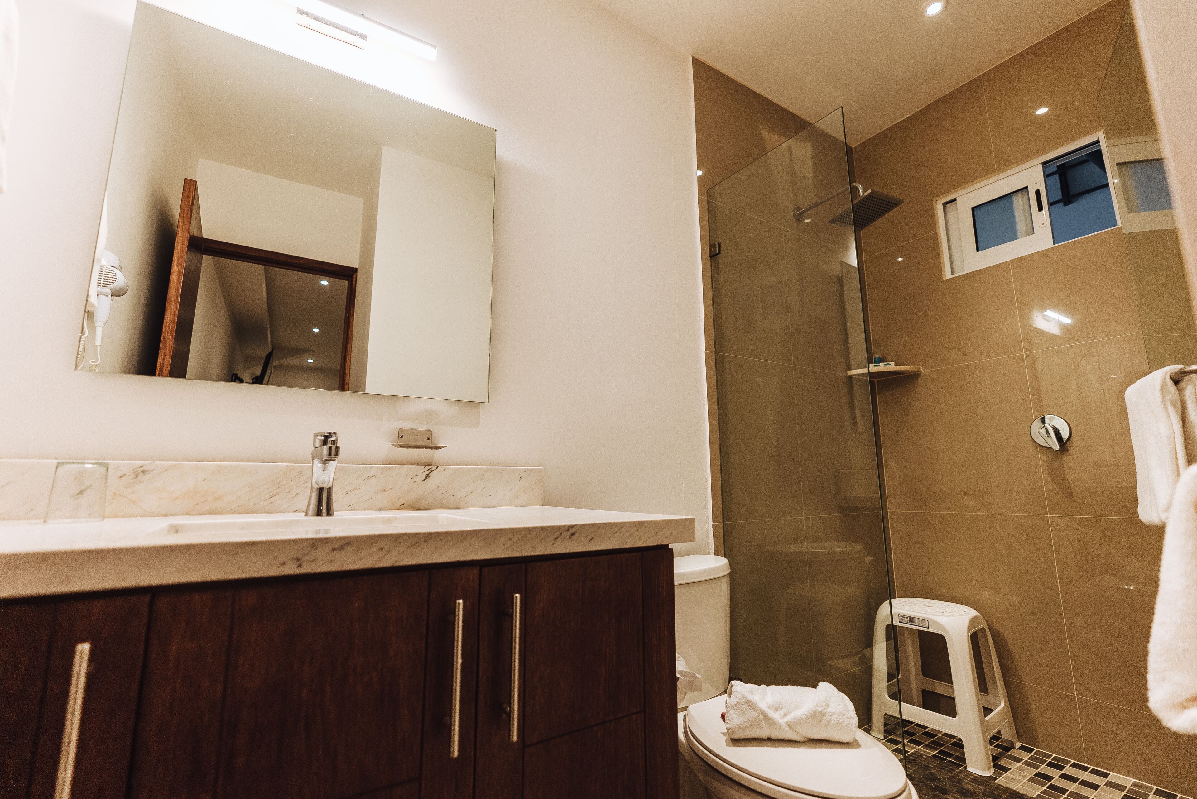 Un baño moderno con un lavabo de mármol, armarios de madera oscura, cabina de ducha de vidrio y un inodoro blanco.