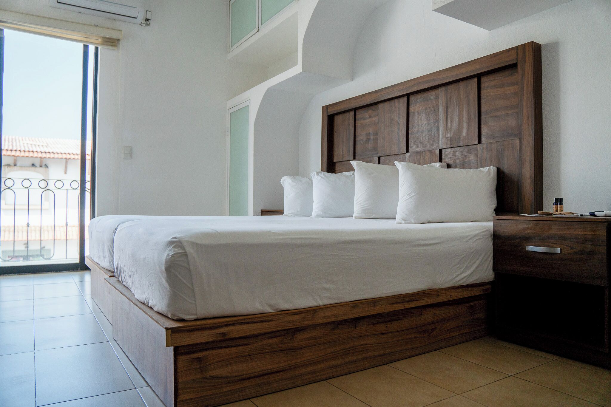 Un dormitorio con cabecera de cama de madera, ropa de cama blanca y una mesita de noche con cajón.