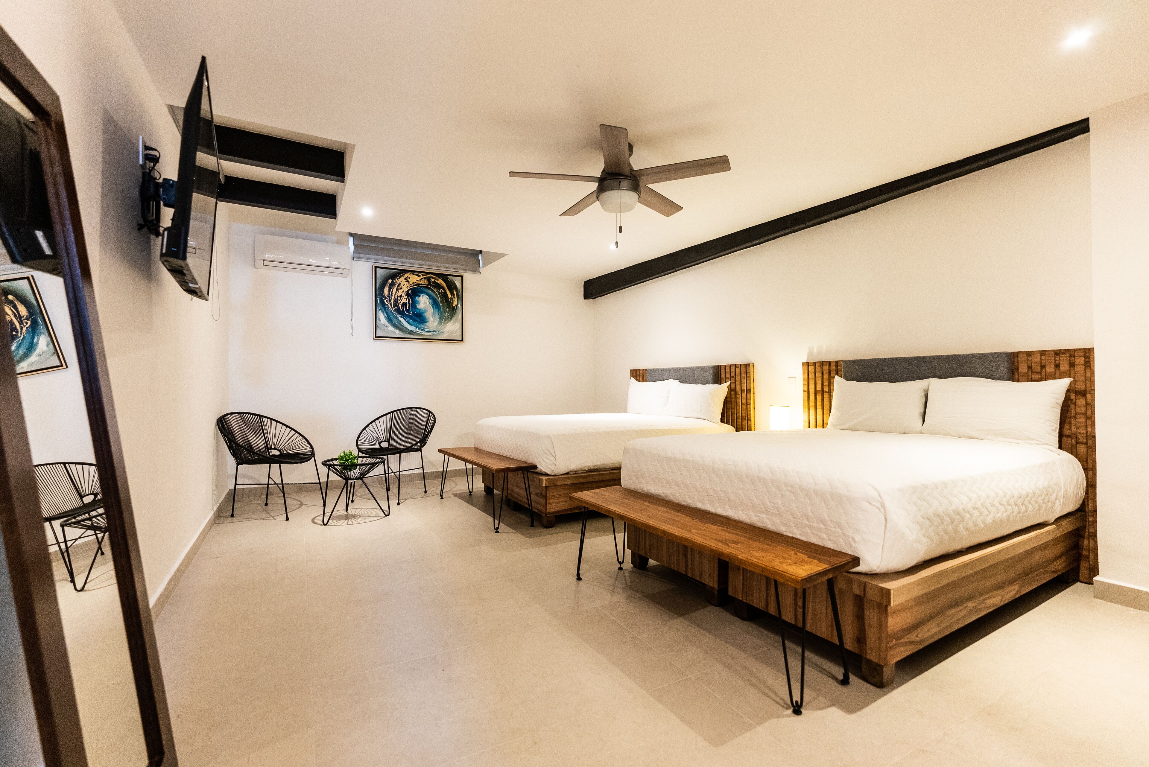 A bedroom with two beds, a ceiling fan, a TV mounted on the wall, and a small seating area with chairs and a table.