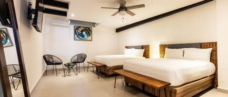A bedroom with two beds, a ceiling fan, a TV mounted on the wall, and a small seating area with chairs and a table.