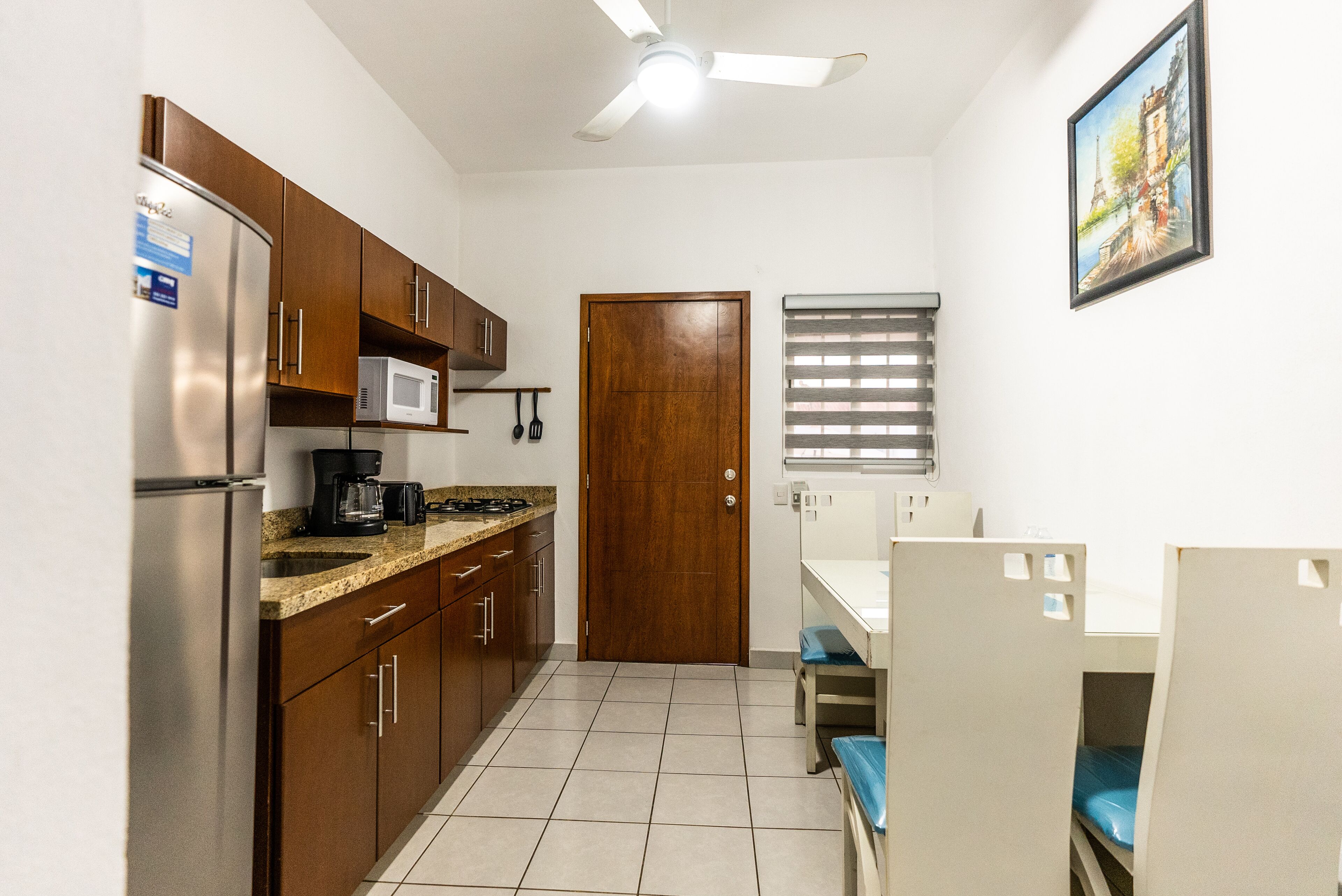 Una cocina compacta con refrigerador, microondas y estufa, una puerta de madera y una ventana con persianas.