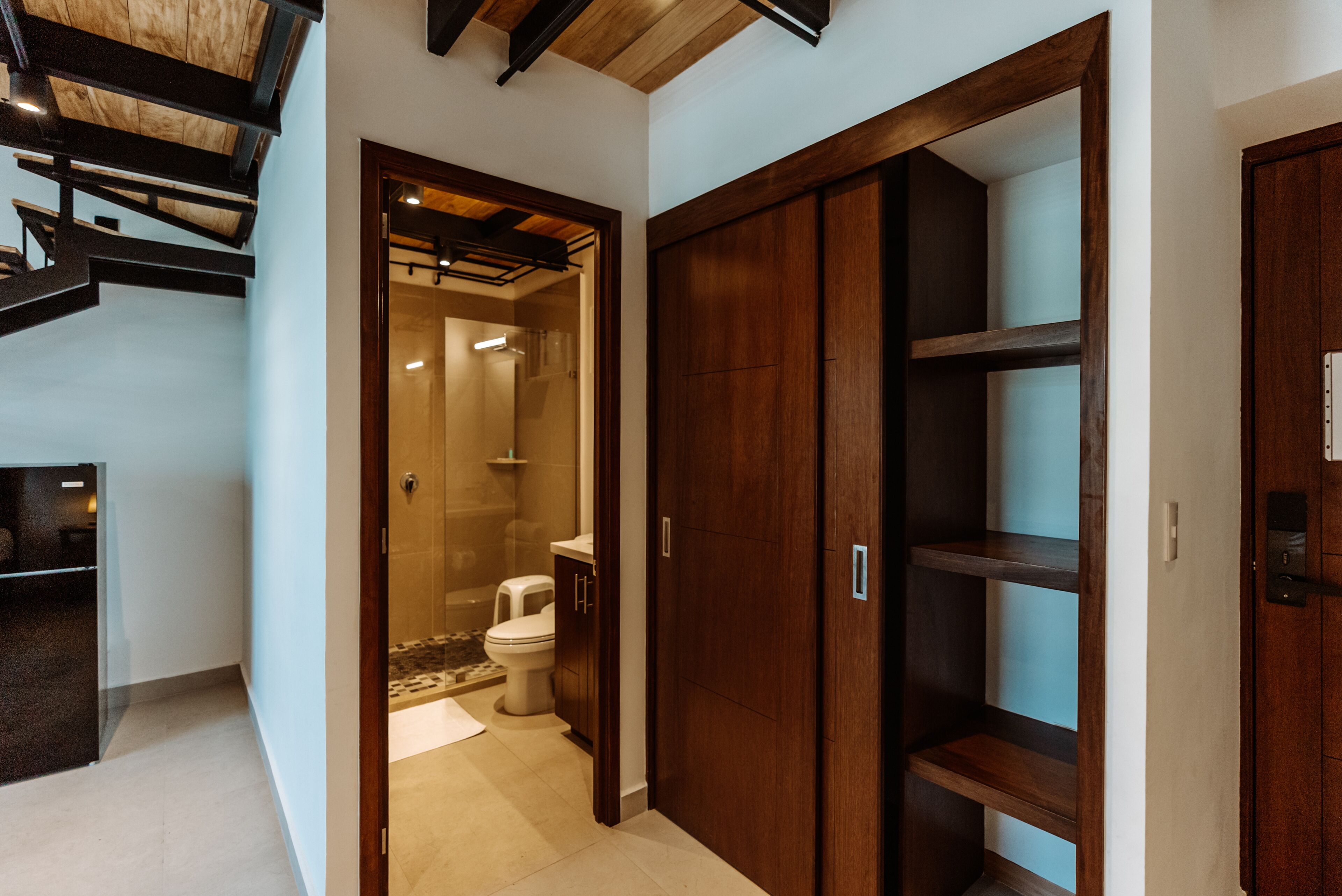 A modern bathroom with a glass shower enclosure, a toilet, and wooden shelving.