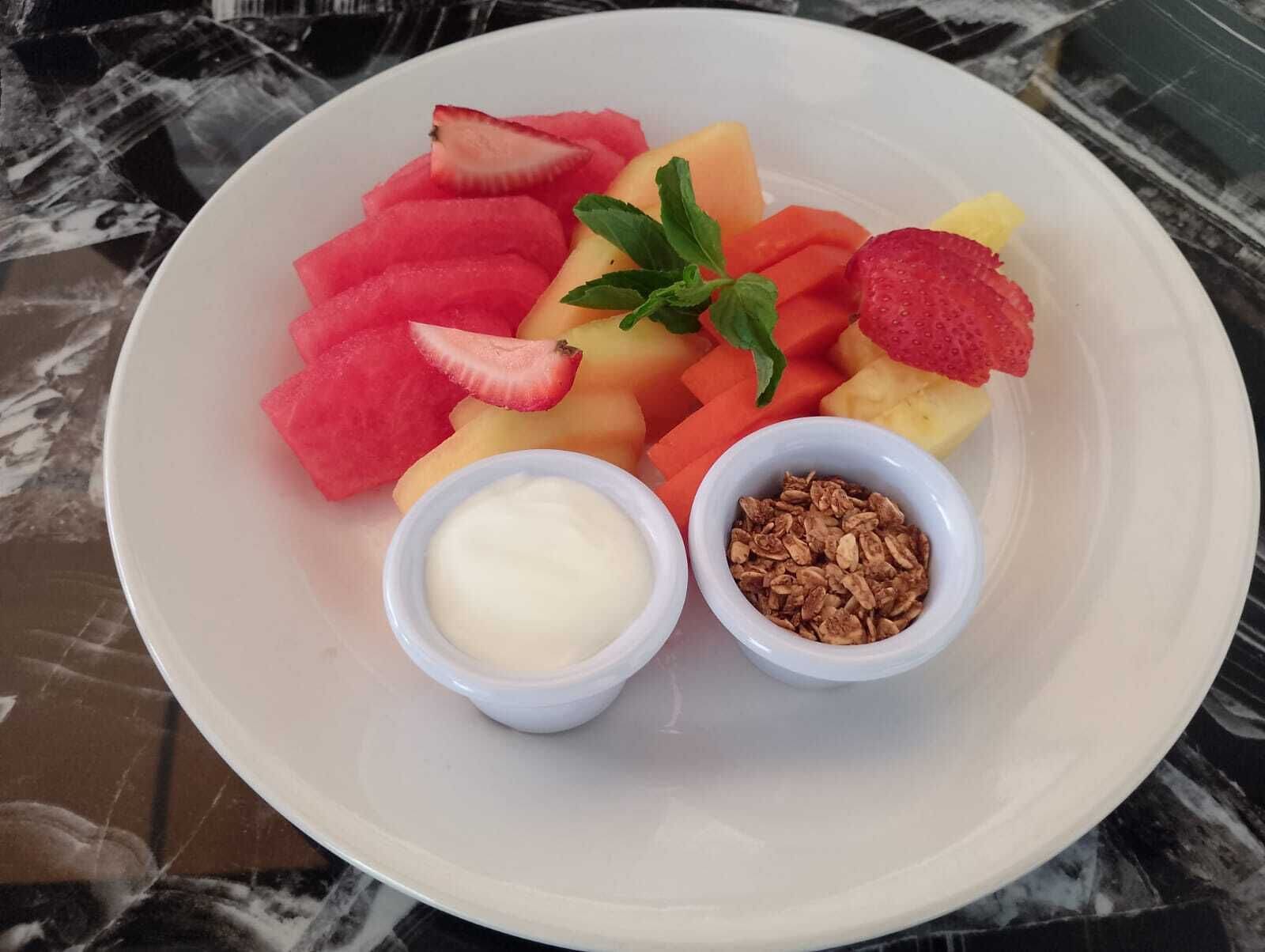 Un plato de frutas cortadas y dos recipientes pequeños con crema y granola.