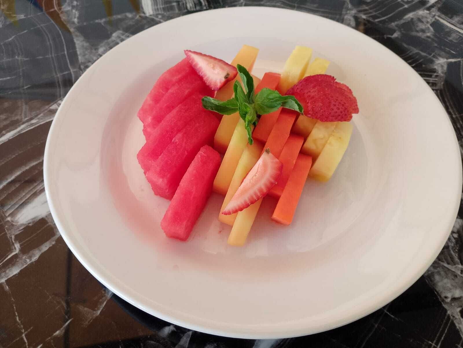 A plate of sliced watermelon, strawberries, and carrots on a marble surface.