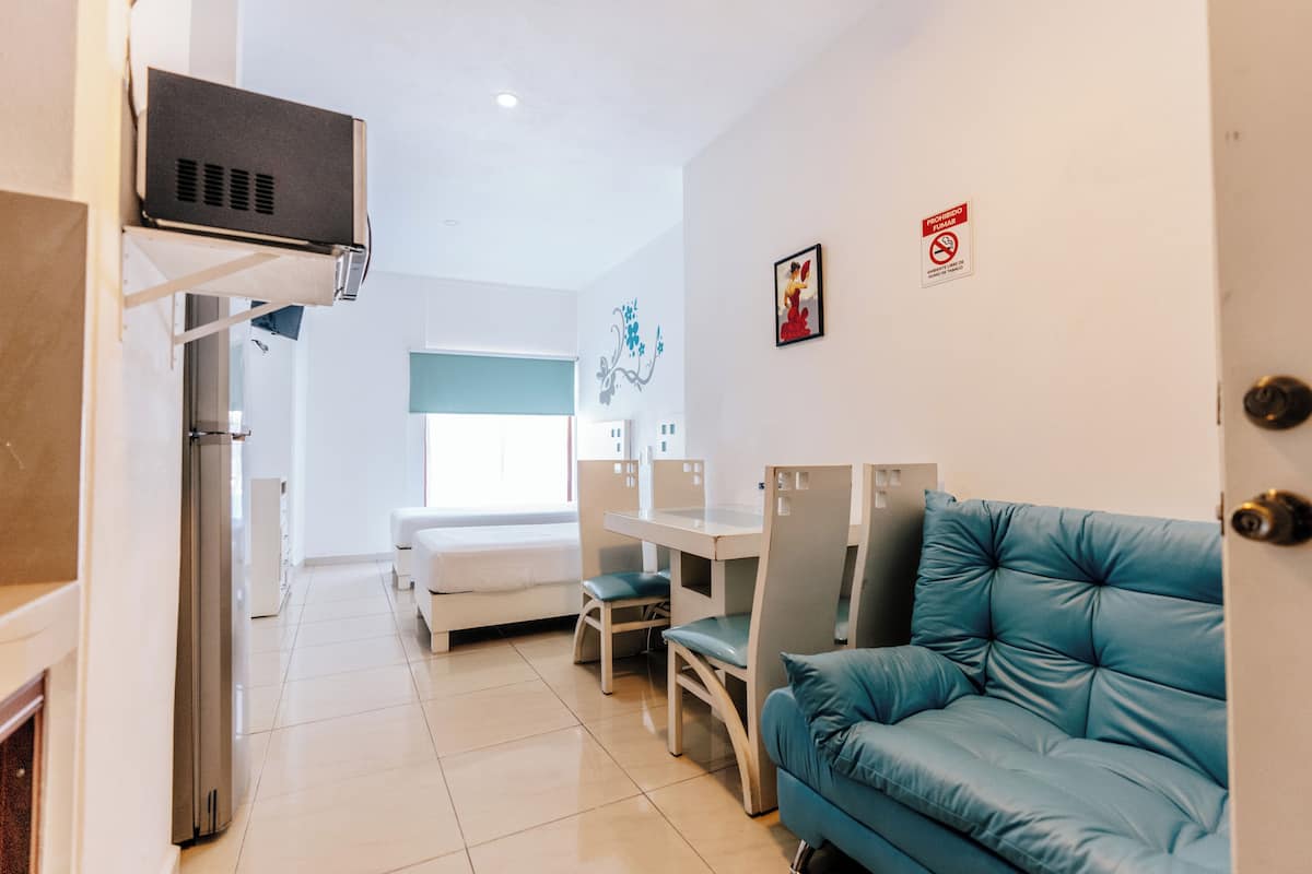 Een moderne hotelkamer met een kitchenette, een blauwe bank, een eettafel en een bed.
