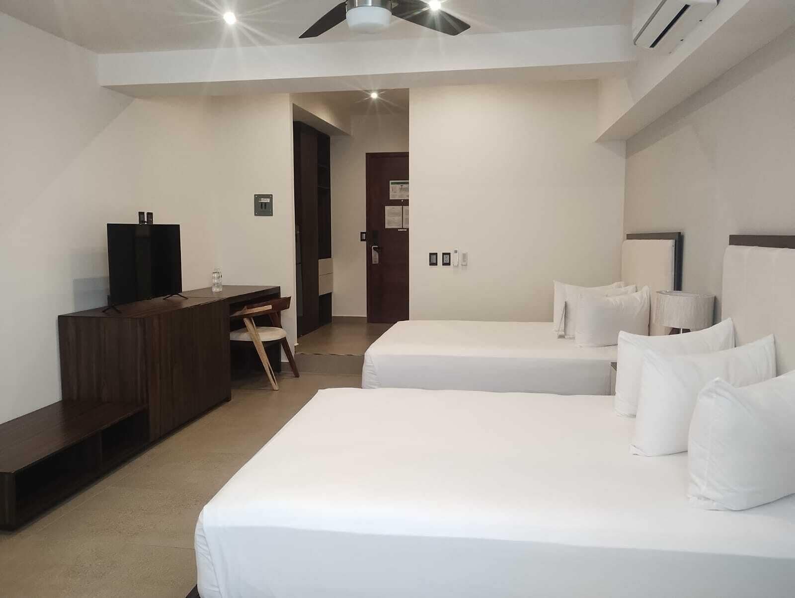 Une chambre d’hôtel avec deux lits simples, un bureau avec une chaise, une télévision et un appareil de climatisation.